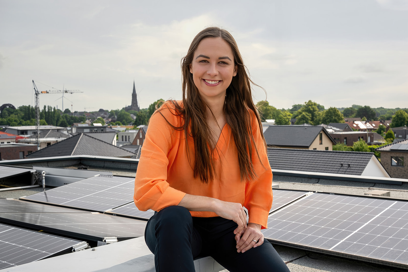 In selbstbewusster und offener Pose sitzt die Bürgermeisterkandidatin auf einem Dach mit Photovoltaikanlage. Im Hintergrund ist der Waldnieler Dom zu sehen.